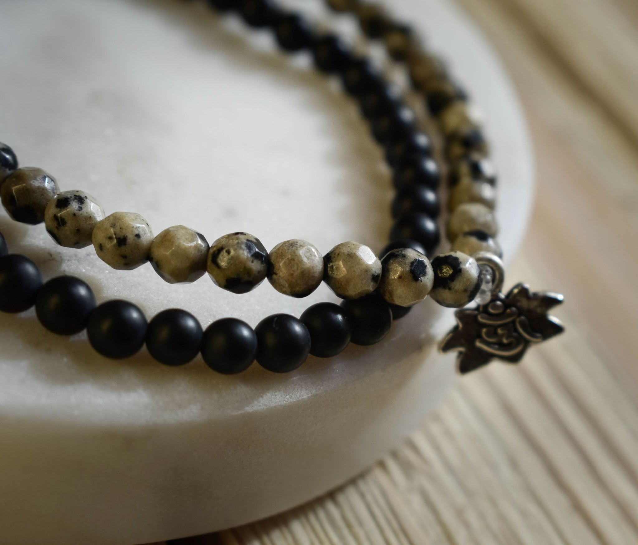Faceted Dalmatian Jasper beads create an earthy, yet upscale modern look. This bracelet comes with a silver lotus charm. Stack them or mix + match your faves! Dalmatian Jasper: as the black + white coloring would suggest, this stone is a powerful balancer of light + dark, yin + yang, or positive + negative. It is known to be helpful in overcoming depression, nightmares, and anxiety. If there is an abundance of negative energy, this stone will do well to transmute those energies into their positive counterpa